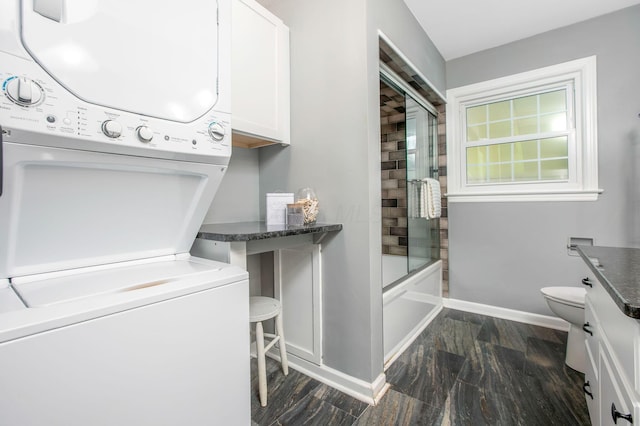 full bath with stacked washer / dryer, baseboards, toilet, shower / bath combination with glass door, and wood finished floors