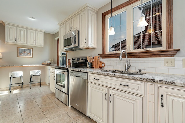 kitchen with hanging light fixtures, appliances with stainless steel finishes, sink, and cream cabinets