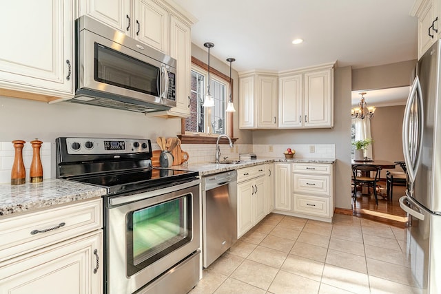 kitchen with appliances with stainless steel finishes, light stone countertops, cream cabinetry, and decorative light fixtures