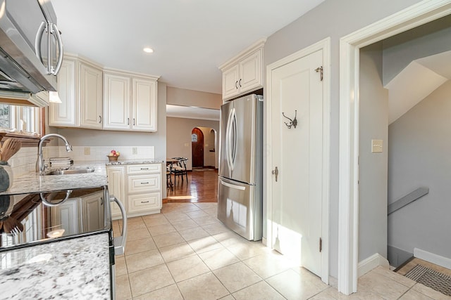 kitchen with appliances with stainless steel finishes, light tile patterned flooring, sink, and light stone countertops