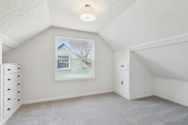 additional living space with a textured ceiling, vaulted ceiling, and light colored carpet