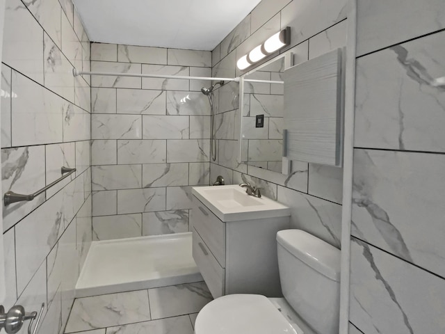 bathroom featuring a tile shower, vanity, tile walls, and toilet