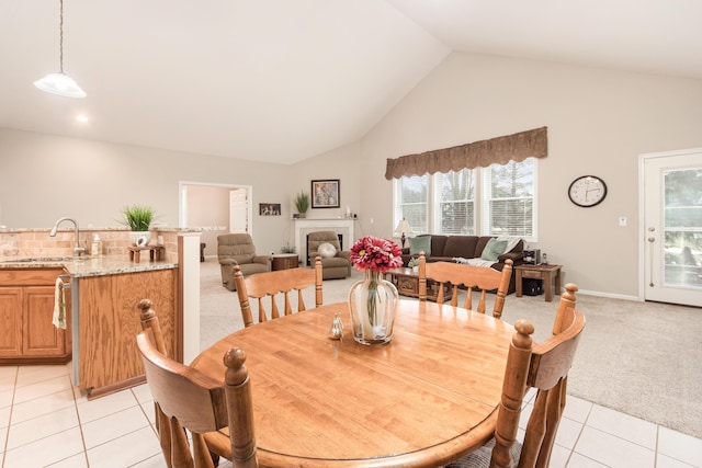 dining room with light tile patterned floors, light carpet, high vaulted ceiling, a tile fireplace, and baseboards