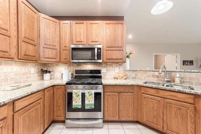 kitchen with light tile patterned floors, decorative backsplash, appliances with stainless steel finishes, a sink, and light stone countertops