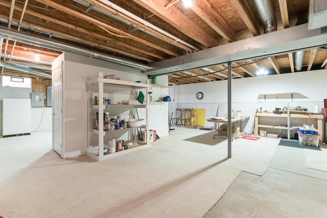 unfinished basement with freestanding refrigerator and electric panel