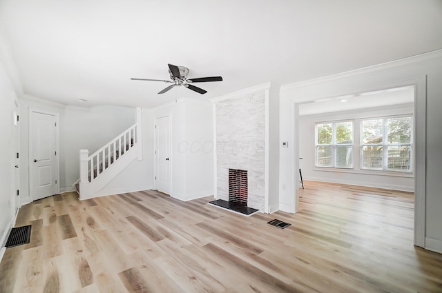 unfurnished living room with light wood-type flooring, crown molding, a stone fireplace, and ceiling fan