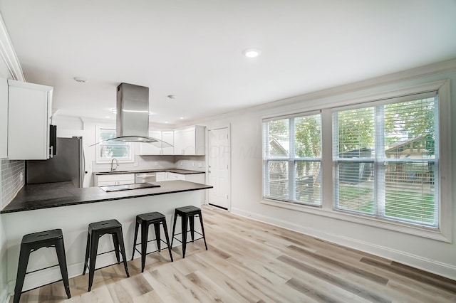 kitchen featuring a kitchen bar, appliances with stainless steel finishes, white cabinetry, island range hood, and kitchen peninsula