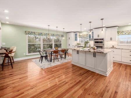 kitchen with decorative light fixtures, double oven, glass insert cabinets, white cabinetry, and a kitchen island