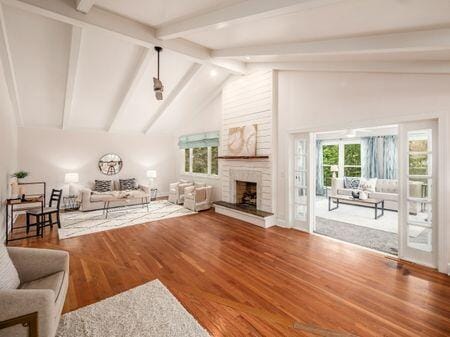 living area with high vaulted ceiling, a fireplace, wood finished floors, and beam ceiling