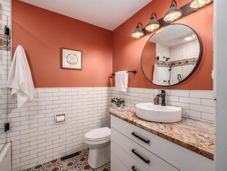 bathroom with a wainscoted wall, tile walls, toilet, vanity, and tiled shower