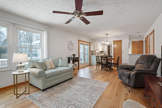 living area featuring light wood-type flooring, ceiling fan, baseboards, and a textured ceiling