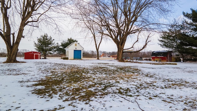 yard layered in snow with an outbuilding, a shed, and a detached garage