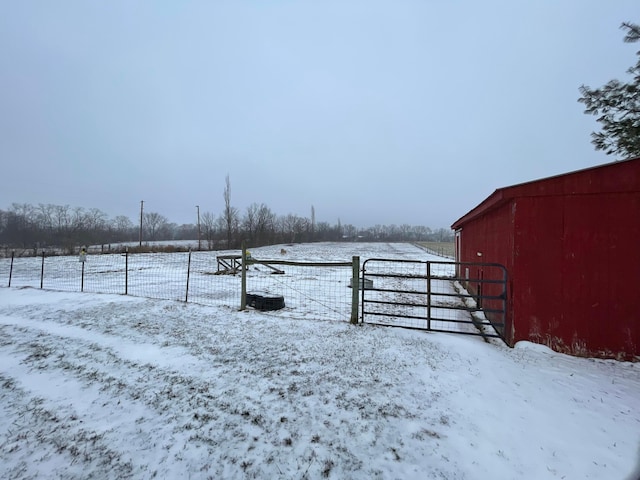 yard covered in snow featuring a garage, a rural view, and fence