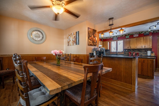 dining area with dark wood-type flooring, wainscoting, wood walls, ceiling fan, and a textured ceiling