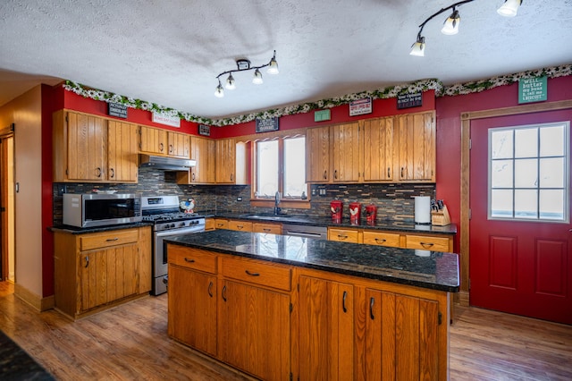 kitchen featuring stainless steel appliances, under cabinet range hood, a kitchen island, and brown cabinets