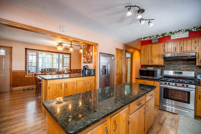 kitchen with under cabinet range hood, stainless steel appliances, a center island, light wood-type flooring, and brown cabinets