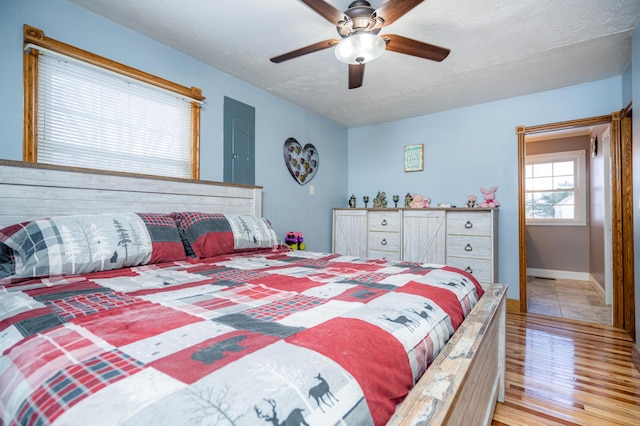 bedroom featuring baseboards, ceiling fan, a textured ceiling, and light wood finished floors