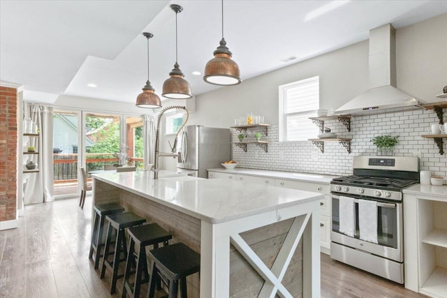 kitchen with hanging light fixtures, stainless steel appliances, white cabinets, a breakfast bar area, and wall chimney exhaust hood