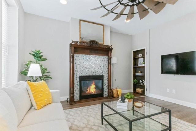 living room featuring hardwood / wood-style flooring, a tile fireplace, built in shelves, and ceiling fan