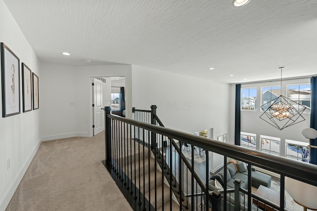 hall with a chandelier, a healthy amount of sunlight, light carpet, and an upstairs landing