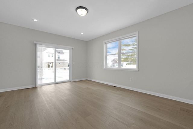 empty room featuring recessed lighting, baseboards, a wealth of natural light, and wood finished floors