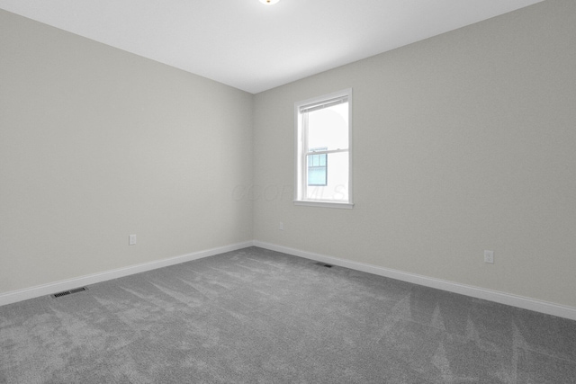 unfurnished room with dark colored carpet, visible vents, and baseboards