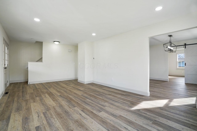 unfurnished room featuring a barn door, baseboards, dark wood-style flooring, stairs, and recessed lighting