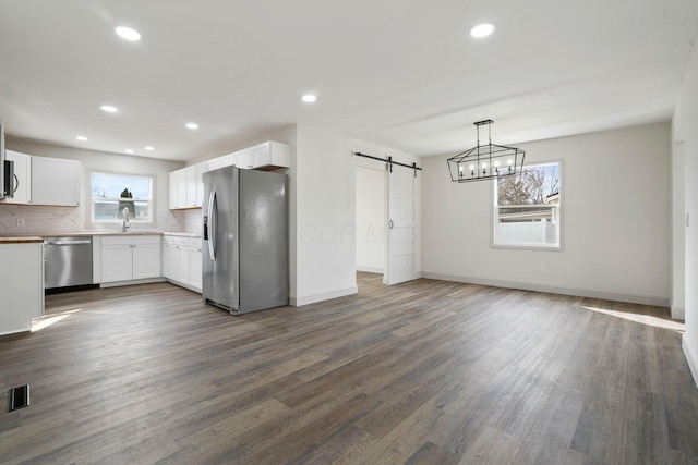 kitchen featuring stainless steel appliances, white cabinets, decorative light fixtures, and a barn door