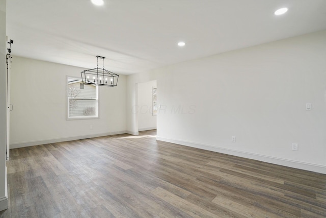 spare room featuring a barn door, baseboards, wood finished floors, and recessed lighting