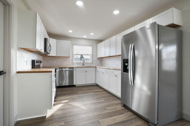 kitchen featuring stainless steel appliances, wood finished floors, white cabinets, wooden counters, and backsplash