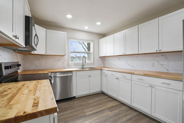 kitchen with butcher block counters, dark wood-type flooring, stainless steel appliances, white cabinetry, and a sink