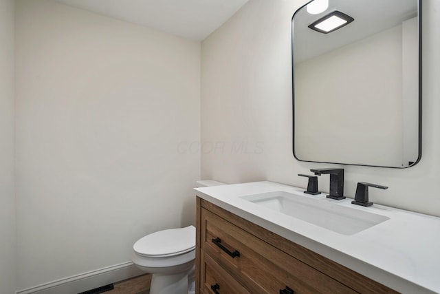 half bath featuring toilet, wood finished floors, and vanity