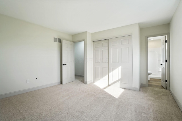 unfurnished bedroom featuring ensuite bathroom, light colored carpet, visible vents, baseboards, and a closet