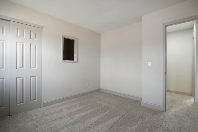 unfurnished bedroom featuring light carpet, baseboards, and a closet