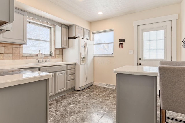 kitchen featuring white refrigerator with ice dispenser, backsplash, gray cabinets, and sink