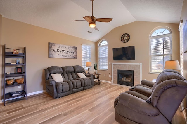 living room with a tile fireplace, light wood-type flooring, lofted ceiling, and ceiling fan