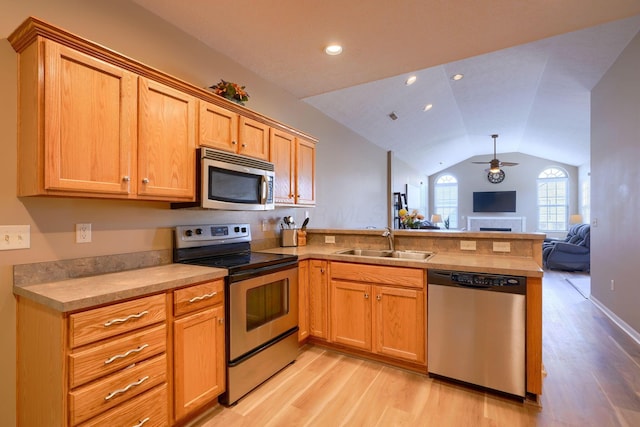 kitchen with appliances with stainless steel finishes, lofted ceiling, sink, light wood-type flooring, and kitchen peninsula