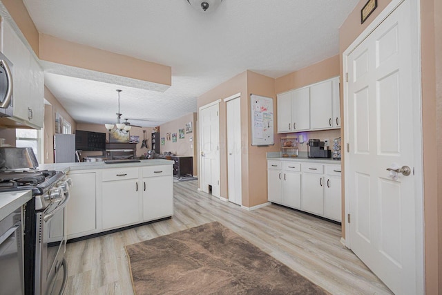 kitchen with light wood-type flooring, white cabinetry, pendant lighting, a textured ceiling, and gas range