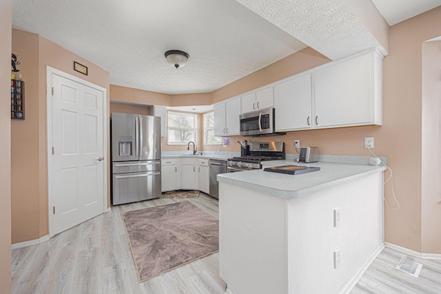 kitchen featuring appliances with stainless steel finishes, light hardwood / wood-style flooring, sink, white cabinetry, and kitchen peninsula