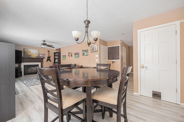 dining area featuring a tile fireplace, light wood-type flooring, and a textured ceiling