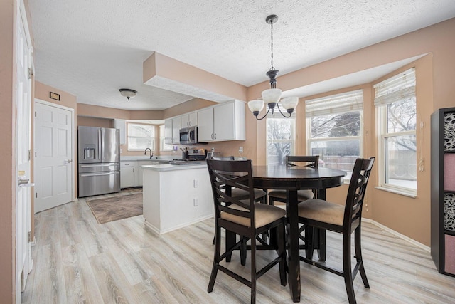 dining area with sink, light wood-type flooring, an inviting chandelier, and a textured ceiling