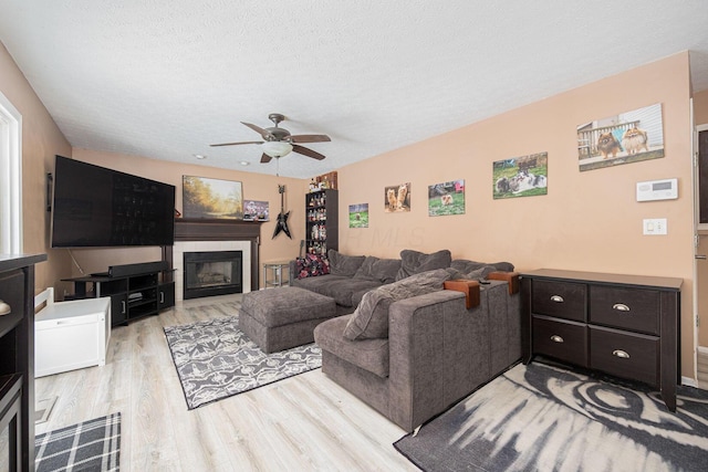 living room featuring light wood-type flooring, a tiled fireplace, a textured ceiling, and ceiling fan