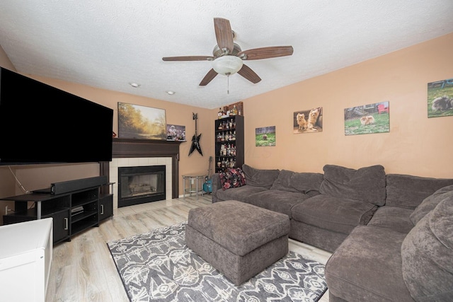 living room featuring ceiling fan, light wood-type flooring, a tile fireplace, and a textured ceiling