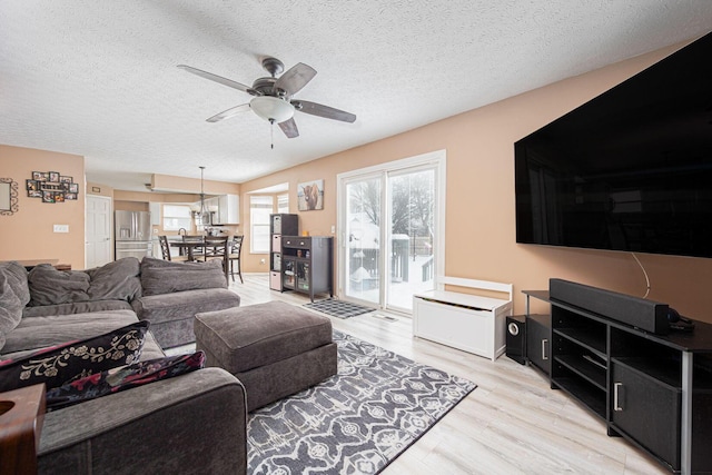 living room featuring ceiling fan, a textured ceiling, and light hardwood / wood-style floors