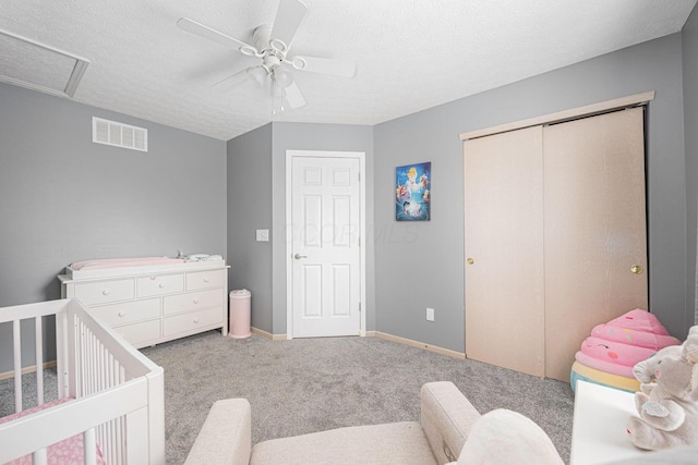 carpeted bedroom with ceiling fan, a closet, a nursery area, and a textured ceiling