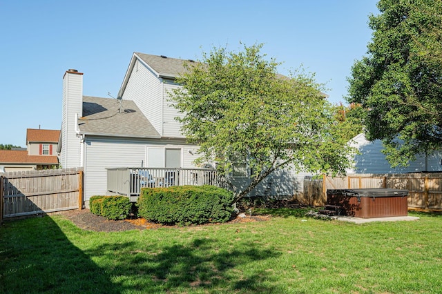 back of property with a hot tub, a lawn, and a wooden deck