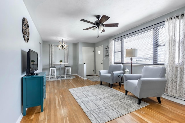 living area with a baseboard radiator, hardwood / wood-style flooring, and ceiling fan with notable chandelier