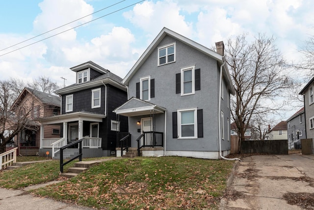 american foursquare style home with a front yard, fence, a chimney, and stucco siding