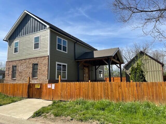 rear view of house featuring brick siding, board and batten siding, and a fenced front yard