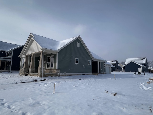 snow covered property featuring a garage, stone siding, a porch, and board and batten siding